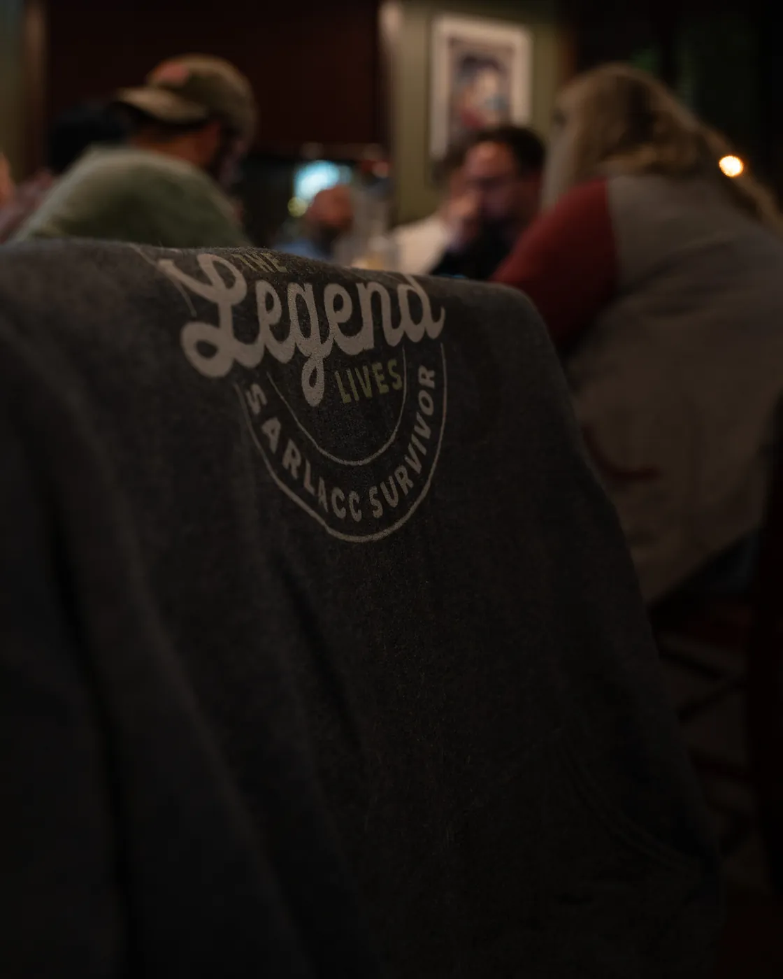 Crowded bar room in warm light with a Legend Lives shirt in the foreground